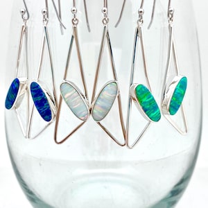 May include: Five pairs of silver triangle earrings with opal stones. The opals are in shades of blue, green, and white.