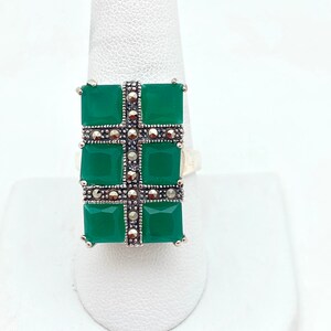 May include: A silver ring with a green stone set in a cross shape. The cross is decorated with small silver accents.