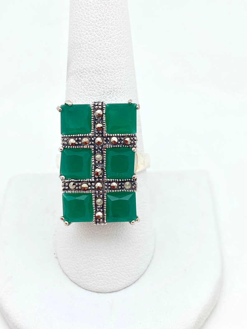 May include: A silver ring with a green stone set in a cross shape. The cross is decorated with small silver accents.