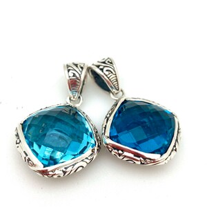May include: Two silver pendants with blue topaz gemstones. The pendants have an ornate silver design around the edges of the gemstones.