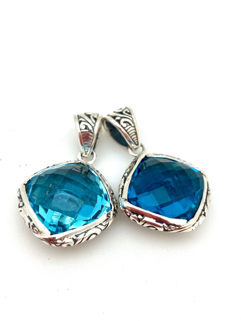 May include: Two silver pendants with blue topaz gemstones. The pendants have an ornate silver design around the edges of the gemstones.