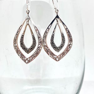 Puede incluir: Pendientes de plata con un delicado diseño de filigrana. Los pendientes presentan dos formas de lágrima, una dentro de la otra, creando un efecto de capas.