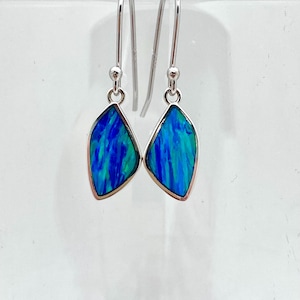 May include: A pair of silver drop earrings featuring blue and green opal stones. The stones are set in a teardrop shape and have a shimmering finish.