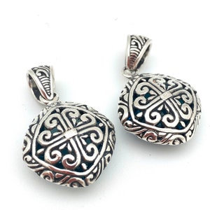 May include: Two silver pendant charms with intricate filigree designs. The charms are square shaped with a blue stone in the center.