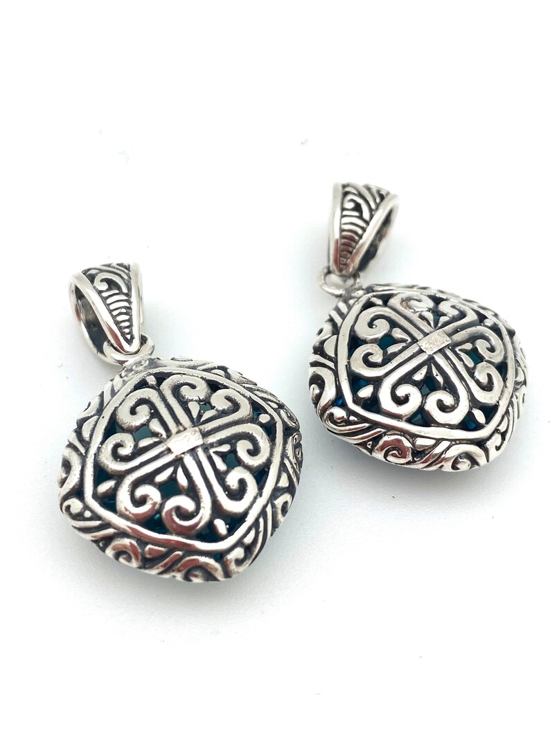 May include: Two silver pendant charms with intricate filigree designs. The charms are square shaped with a blue stone in the center.