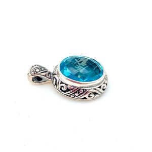 May include: A silver pendant with an ornate design featuring a large, round, light blue gemstone.