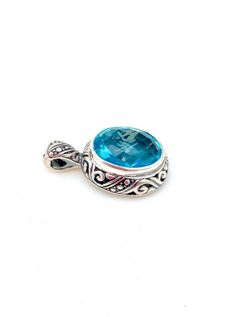 May include: A silver pendant with an ornate design featuring a large, round, light blue gemstone.