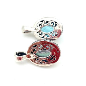 May include: Two silver pendants with ornate filigree designs. Each pendant features a light blue oval gemstone.