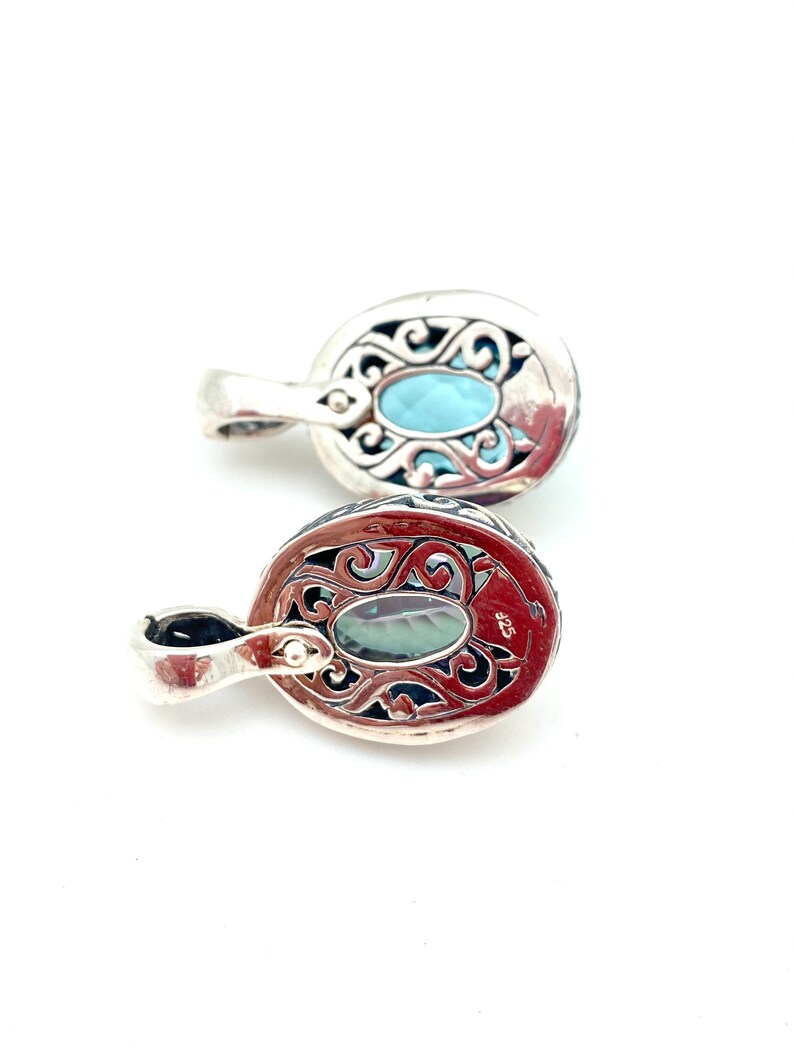 May include: Two silver pendants with ornate filigree designs. Each pendant features a light blue oval gemstone.