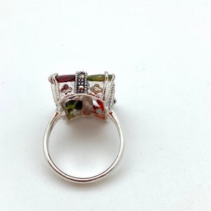May include: A silver ring with a multi-colored stone set in a filigree design. The stone is surrounded by a band of black marcasite.