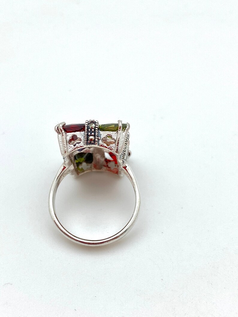 May include: A silver ring with a multi-colored stone set in a filigree design. The stone is surrounded by a band of black marcasite.