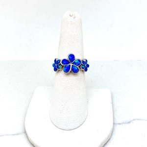 May include: A silver ring with blue opal flower accents. The ring is displayed on a white ring stand.