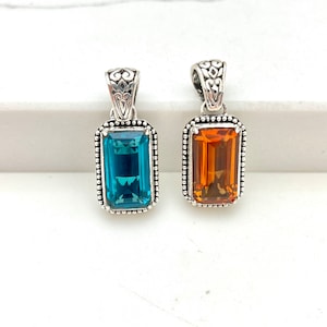 May include: Two silver pendants with ornate details, one with a blue gemstone and the other with an orange gemstone.