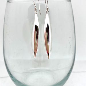 May include: A pair of silver dangle earrings with a smooth, teardrop-shaped design.
