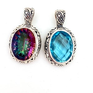 May include: Two silver pendants with oval-shaped gemstones. The pendant on the left has a rainbow mystic topaz gemstone. The pendant on the right has a light blue topaz gemstone.