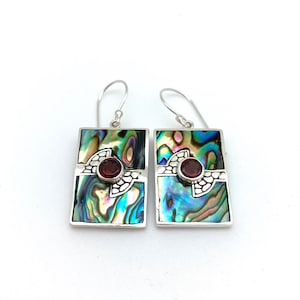 May include: A pair of silver earrings with a rectangular abalone shell design and a red gemstone accent.