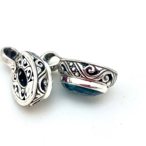 May include: A silver pendant with an ornate design and a blue gemstone. The pendant is made of sterling silver and features a detailed floral pattern.