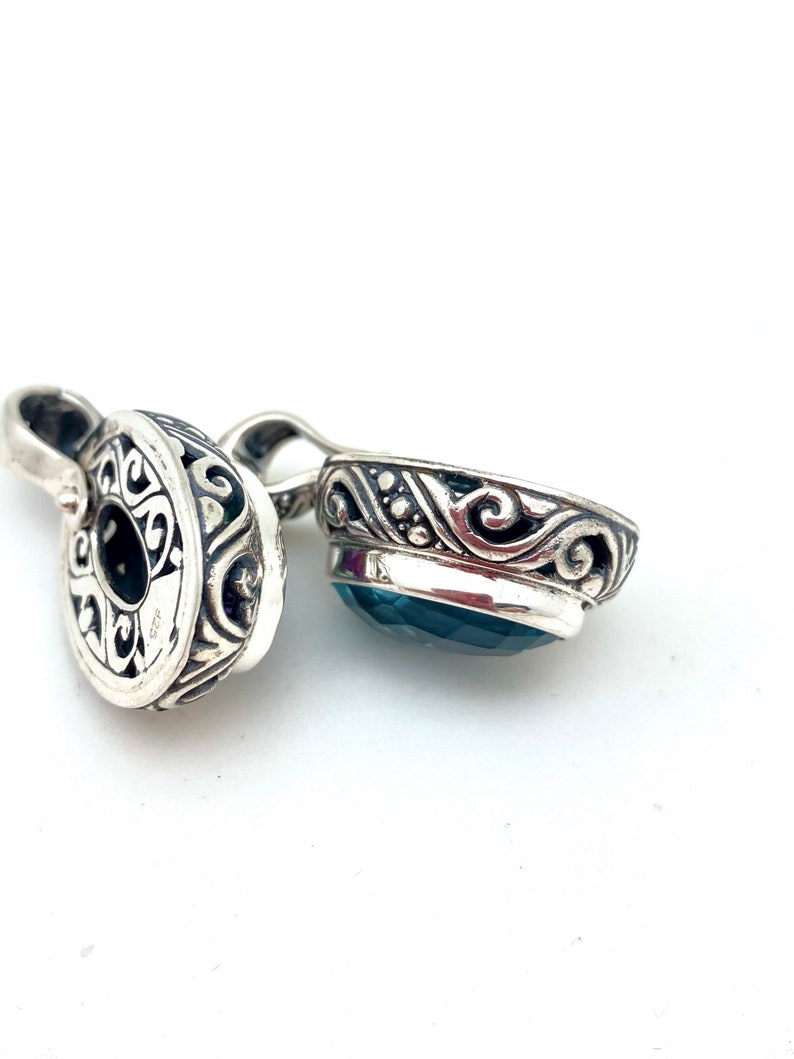 May include: A silver pendant with an ornate design and a blue gemstone. The pendant is made of sterling silver and features a detailed floral pattern.