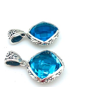 May include: Two silver pendants with a blue gemstone in a square shape. The pendants have an intricate silver design around the gemstone.