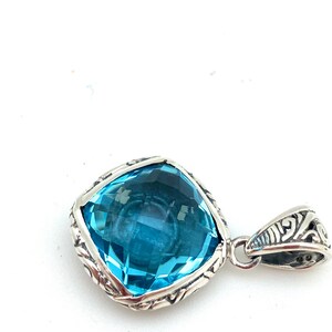 May include: A silver pendant with a large, square-shaped, light blue topaz gemstone. The pendant has an intricate, detailed design around the gemstone.