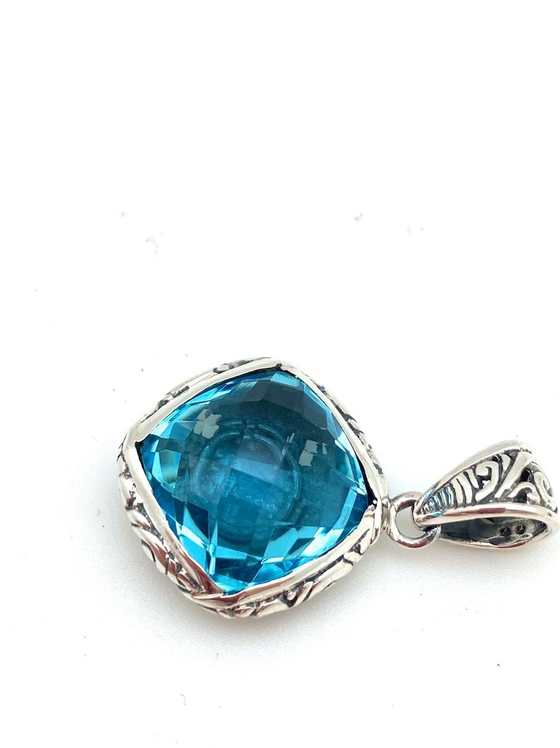May include: A silver pendant with a large, square-shaped, light blue topaz gemstone. The pendant has an intricate, detailed design around the gemstone.