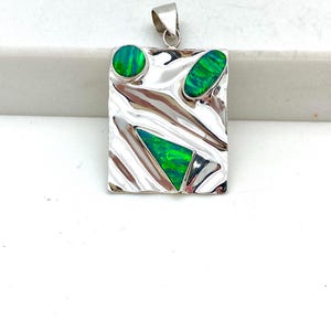 May include: A silver pendant with a textured rectangular design featuring three green opal stones in different shapes.