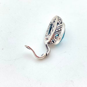 May include: A silver earring with a blue gemstone set in an ornate silver setting. The earring has a hook closure.