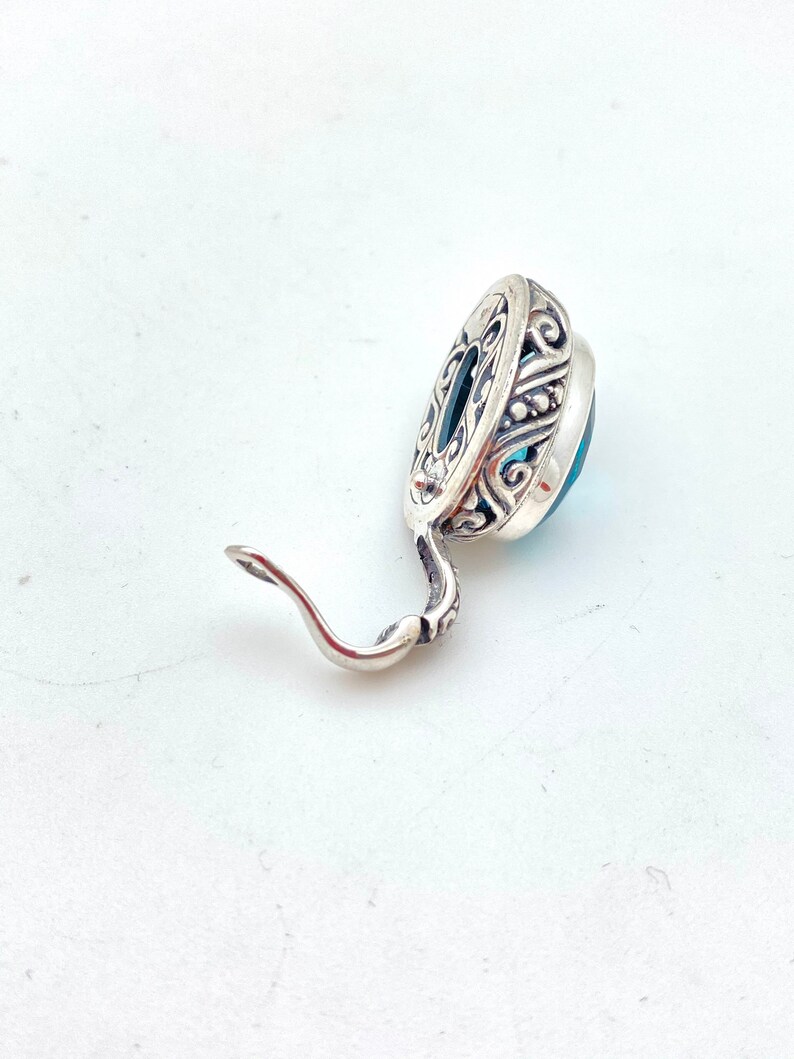 May include: A silver earring with a blue gemstone set in an ornate silver setting. The earring has a hook closure.