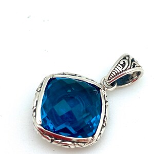 May include: A silver pendant with a large, square, blue gemstone set in a detailed silver frame.