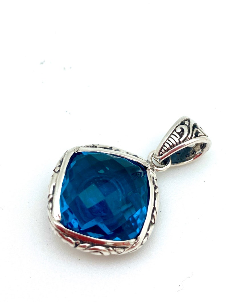 May include: A silver pendant with a large, square, blue gemstone set in a detailed silver frame.