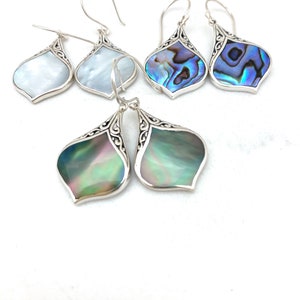 May include: A set of three pairs of silver earrings with abalone shell accents. The earrings are in the shape of a teardrop with an intricate design. The abalone shell is iridescent and comes in shades of blue, green, and white.