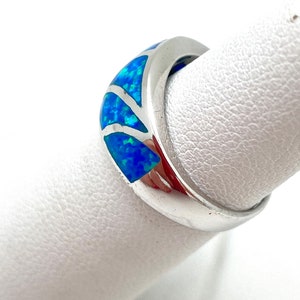 May include: A silver band ring with a blue opal inlay. The opal is set in a curved design and has a light blue and green color.