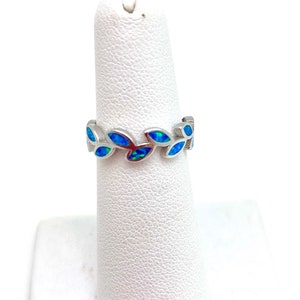 May include: A silver ring with a band of blue opal leaves. The ring is on a white ring display stand.