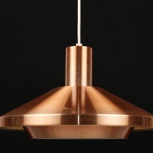 May include: A copper pendant light with a wide, flat, circular shade. The shade has a slight curve to it, giving it a modern look.