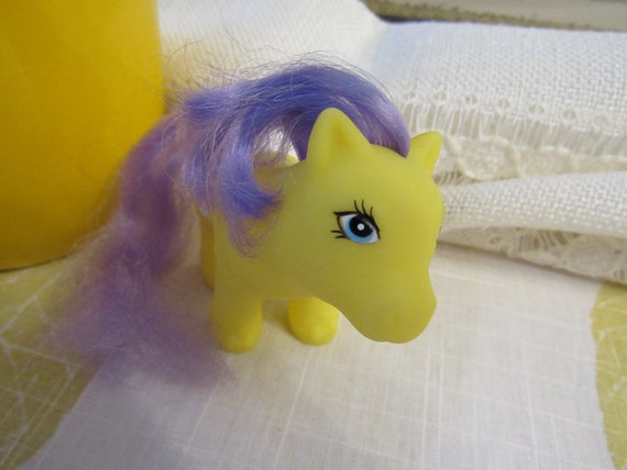 Petit poney jaune aux cheveux violets, yeux bleus et couche