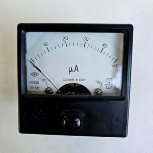 Può includere: Un microamperometro analogico nero con quadrante bianco, dotato di una lancetta che punta vicino allo zero, una scala da 0 a 50, il simbolo μA e il testo M2001, III-81r., e СДЕЛАНО В СССР stampato sul quadrante. Il dispositivo ha una cornice quadrata.