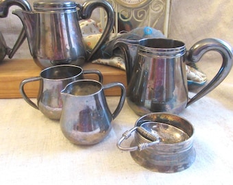 May include: A collection of antique silver tea service items, including a teapot, creamer, sugar bowl, and tea strainer. The pieces have curved handles and a reflective surface, suggesting they are made of silver or a similar metal.