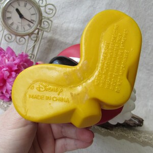 Puede incluir: Pie amarillo de una figura de Disney, con el texto "Disney MADE IN CHINA" visible. La figura tiene un dise&ntilde;o rojo y negro. La parte inferior del pie tiene el texto "NOT DISHWASHER SAFE WASH THOROUGHLY BEFORE USING WASH IN WARM WATER ONLY AVOID TEMPERATURE EXTREMES DO NOT MICROWAVE."