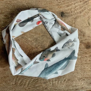 May include: White fabric headband with a colorful fish print. The headband is rolled up and shows a variety of fish species, including trout, catfish, and bass.