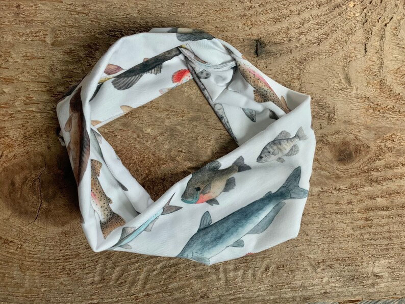 May include: White fabric headband with a colorful fish print. The headband is rolled up and shows a variety of fish species, including trout, catfish, and bass.