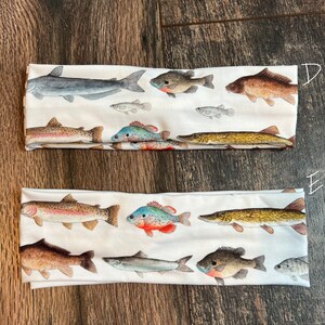 May include: Two white headbands with a variety of colorful fish printed on them. The fish are in different sizes and positions, and some are facing left while others are facing right. The headbands are made of a soft, stretchy material and are perfect for keeping your hair out of your face.