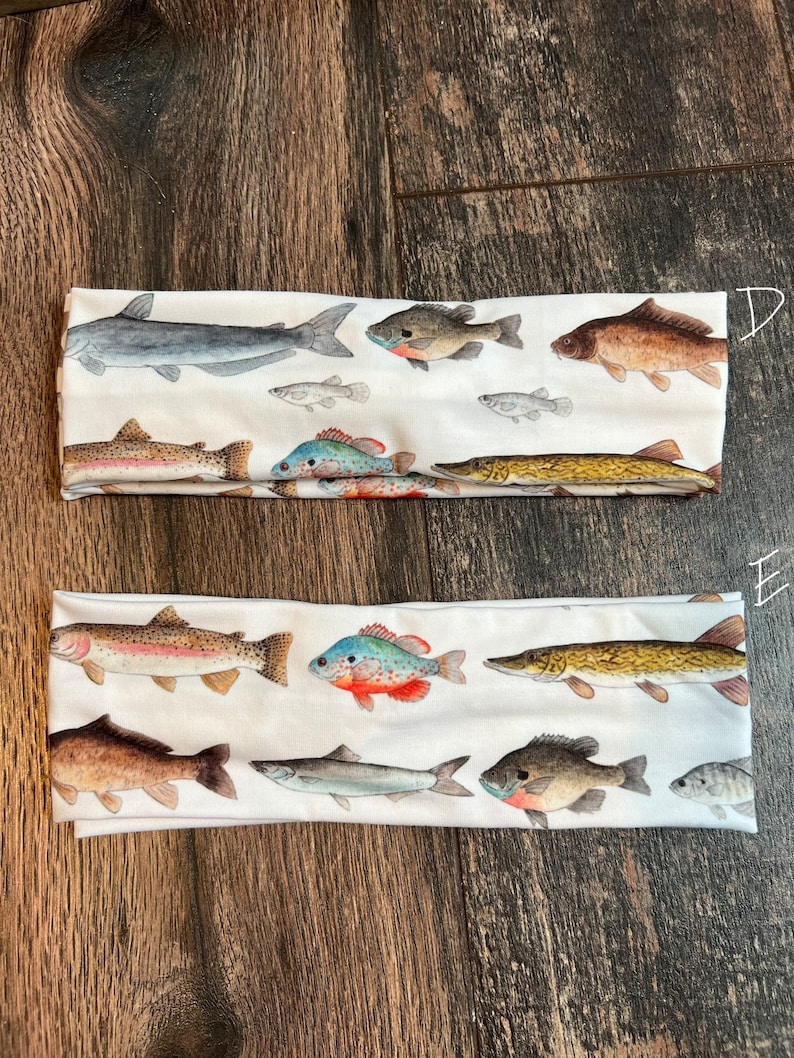 May include: Two white headbands with a variety of colorful fish printed on them. The fish are in different sizes and positions, and some are facing left while others are facing right. The headbands are made of a soft, stretchy material and are perfect for keeping your hair out of your face.