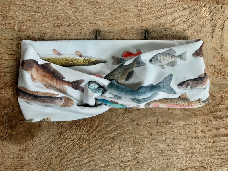 May include: A white headband with a colorful fish print. The headband is made of a soft, stretchy fabric and is perfect for keeping hair out of your face.