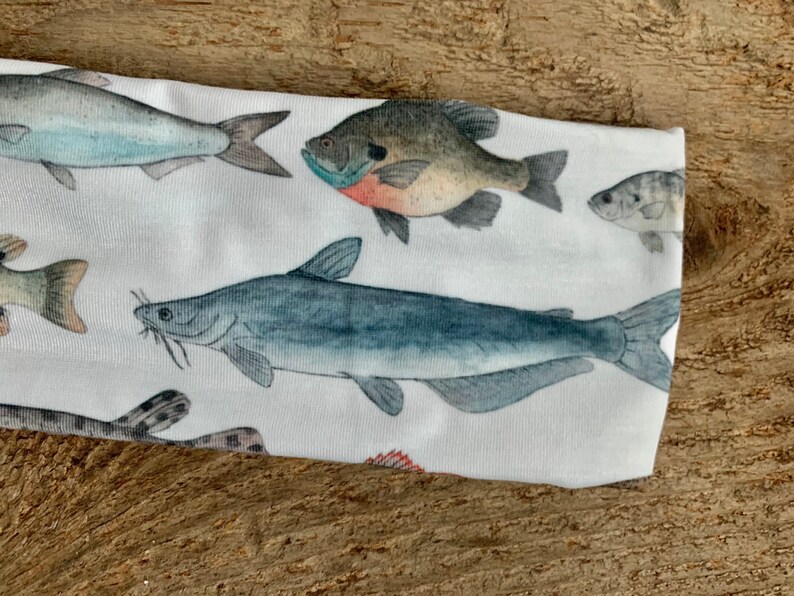 May include: White headband with a colorful fish print. The fish are illustrated in a realistic style and include a catfish, a bass, and a perch.