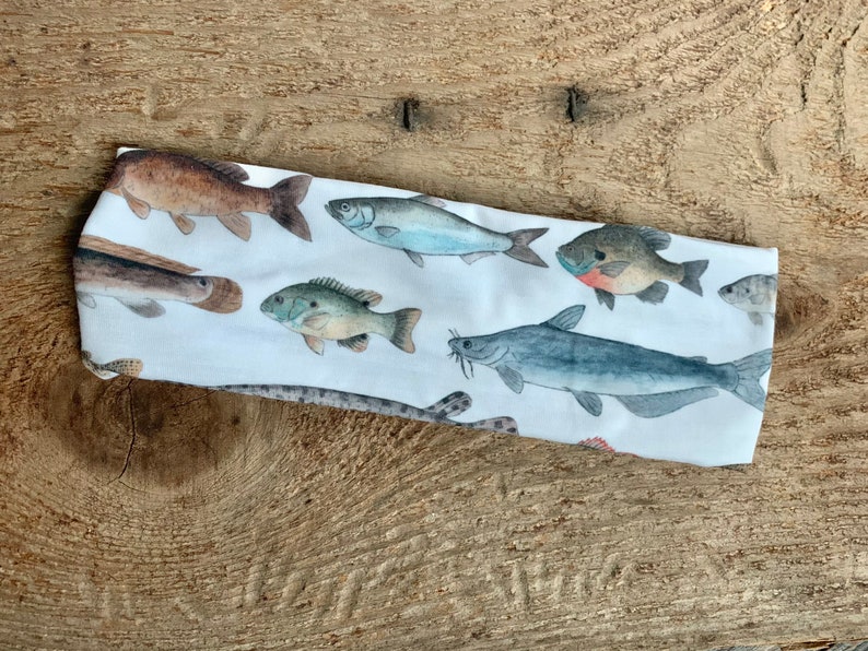 May include: White headband with a colorful fish print. The fish are various species, including catfish, bass, and sunfish.