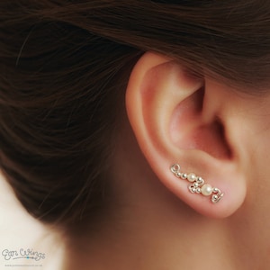 May include: A silver ear cuff with a delicate design featuring small white pearls. The cuff is worn on the upper part of the ear, just above the lobe.