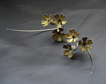 Puede incluir: Una rama de plata delicada con cinco flores de metal amarillo. Las flores están dispuestas en un racimo en el extremo de la rama, con el otro extremo de la rama extendiéndose hacia la izquierda.