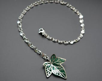 May include: Silver-toned necklace with a green leaf pendant. The leaf pendant has a detailed, openwork design with a green enamel filling. The chain is delicate and the clasp is visible.