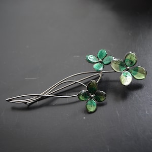 May include: A silver brooch featuring three green enamel flowers. The flowers are clustered together and have a delicate, whimsical design.
