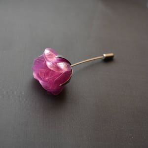 May include: A purple glass rose pin with a silver stem. The rose is made of layered petals and has a delicate, feminine look.